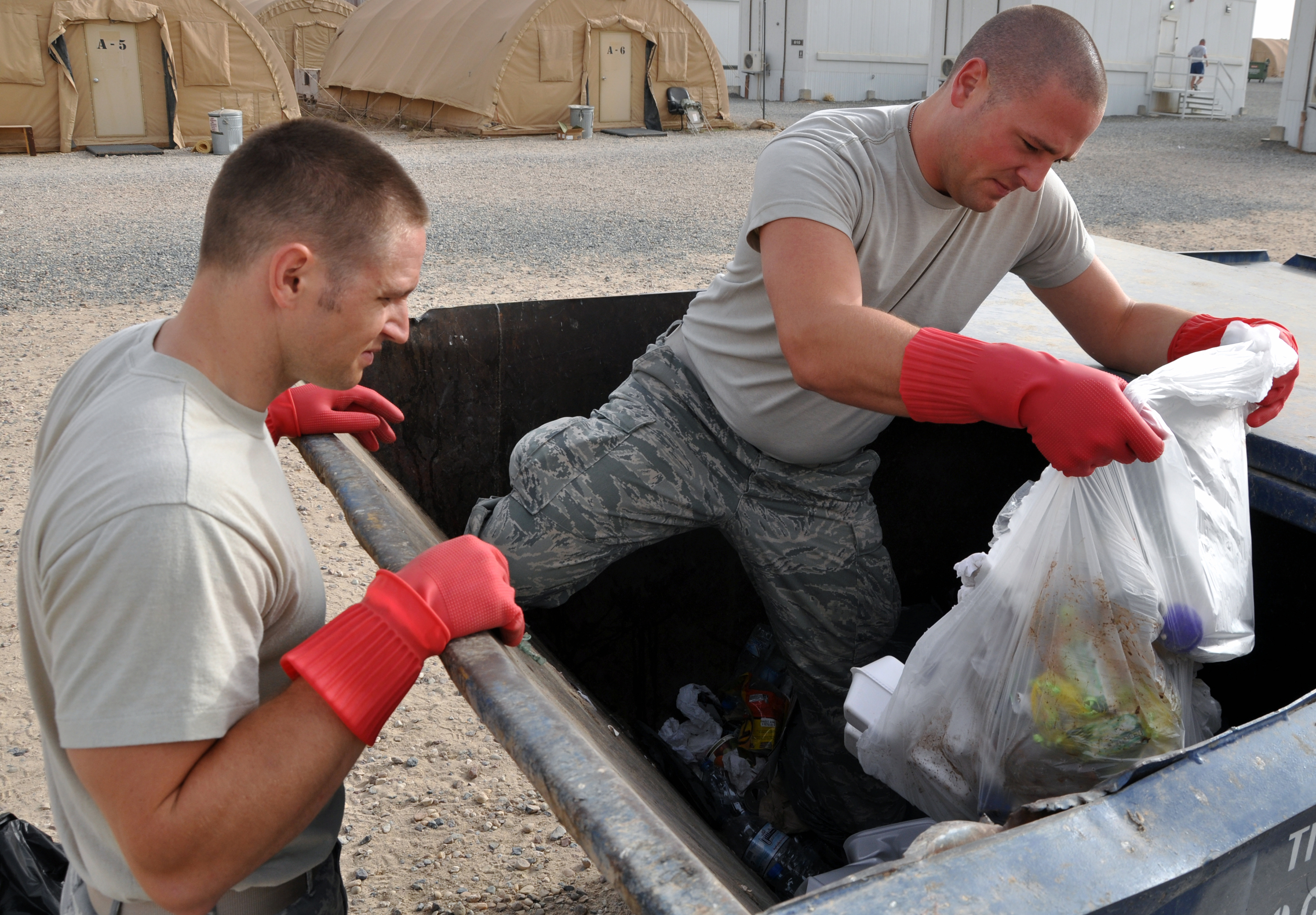 Two men in fatigues, one standing in the garbage bin