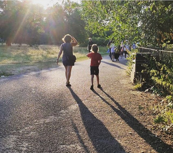 Mother and son walking away from the camera in a park, with long shadows behind them