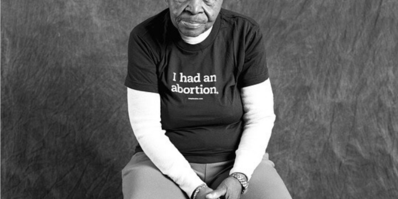 A Black woman in her 80s wearing a t-shirt that says "I had an abortion."