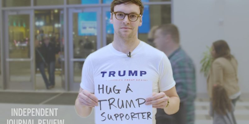 white man holding a sign that says "hug a Trump supporter"