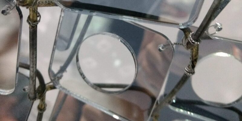 A closeup of art that has tiny mirrors with circles cut out woven into a chainlink fence