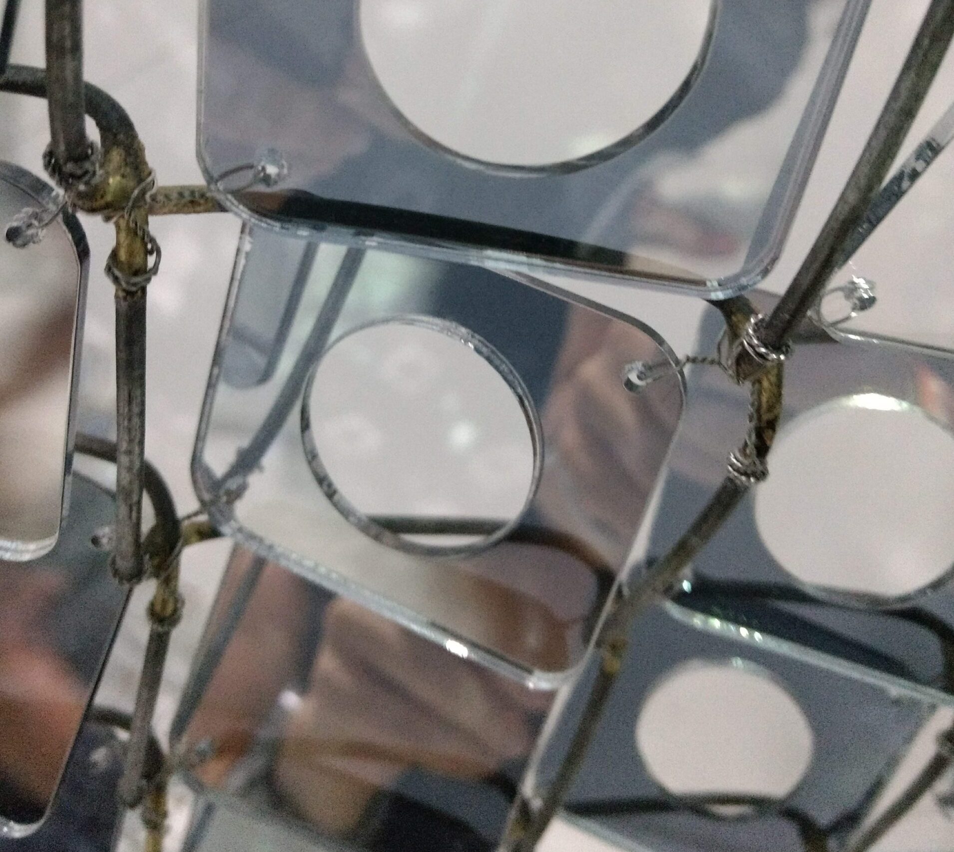 A closeup of art that has tiny mirrors with circles cut out woven into a chainlink fence